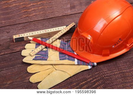 Orange hard hat and gloves for work on wood background