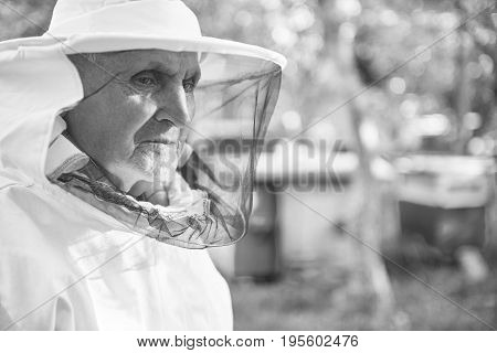 Monochrome shot of an elderly man in beekeeping suit looking away standing outdoors copyspace worker professional beekeeper apiculture farmer farming concept.
