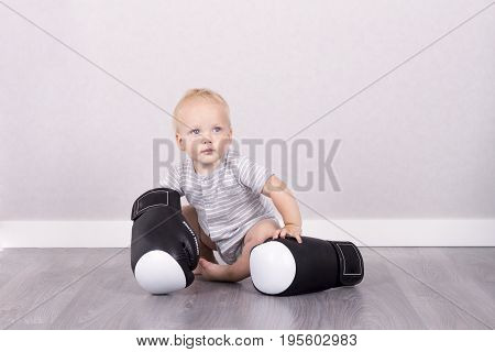 Cute baby boy in boxing gloves against the grey background.
