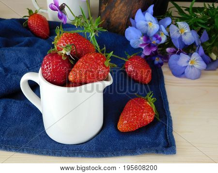 Fresh ripe strawberries in a ceramic jug surrounded by flowers and berries