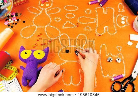 Workplace of a tailor: fabric spools measuring tape buttons needles bows toys and drawings. Girl putting black buttons on the place of rabbit eyes.