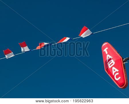 Editorial Les Loges, France - July 07, 2017: French flags erected ready to celebrate Bastille Day (Fête Nationale) and a Tabac sign sign indicating a retail outlet for cigarettes and tobacco seen in the village of Les Loges, Normandy.