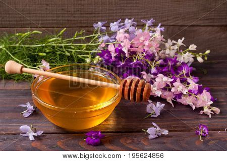 Jar of honey with wildflowers on a dark wooden background.
