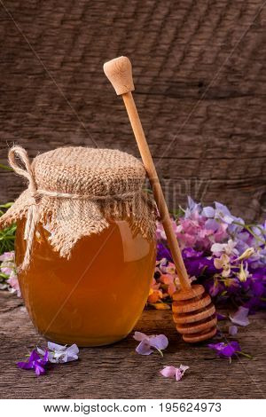 Jar of honey with wildflowers on old wooden background.