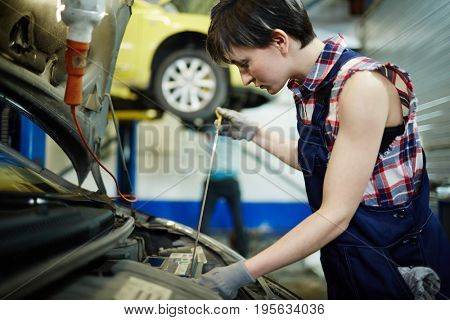 Woman technician checking or tuning car engine in garage