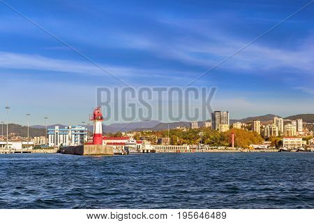 Lighthouse on edge of breakwater in Sochi sea port. Luxury yachts and private boats moored at pier. In background architecture modern resort town hotels and sanatoriums. Sochi Krasnodar Russia