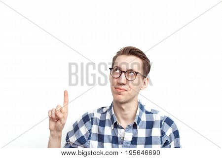Young man in checkered shirt and glasses pointing up on white background.