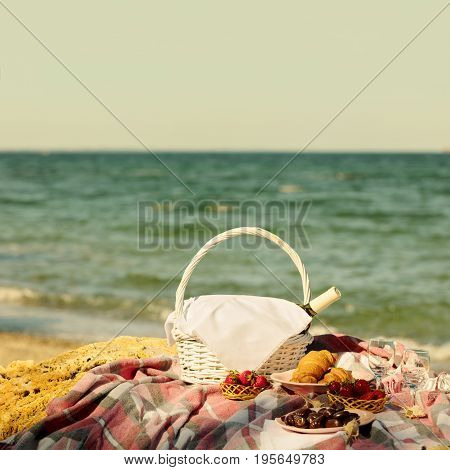 Summer time at the sea. Romantic picnic on the beach - wine strawberries and sweets. Selective focus.