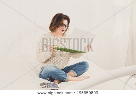 Young woman freelancer works at home in bed with laptop. Engrossed Girl in eyeglasses. Freelance.