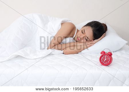 young woman on white bed yawn awakening tired holding alarm clock. lazily don't want to wake up.