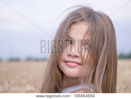 A beautiful 8-year-old girl with long hair and green eyes in a golden wheat field at a summer day
