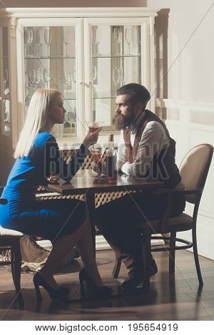 Woman and man dating in restaurant. Girl with blond hair and hipster drinking wine from martini glasses. Couple in love. Alcohol and appetizer. Addictive and convive. Unhealthy lifestyle. Bad habits