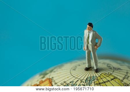 miniature businessman standing on top of the globe map with blue background copy space.