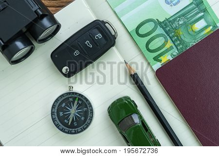 car key compass pencil with passport euro banknote on paper note and miniature car as travel planning road trip concept.