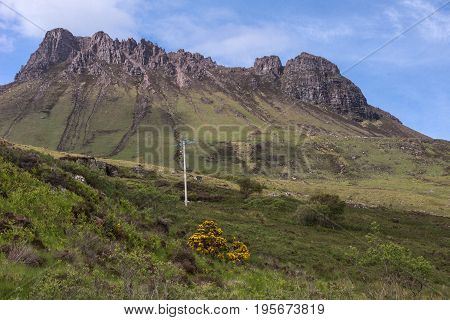 Assynt Peninsula Scotland - June 7 2012: Brown Mountain ridge along Loch Lurgainn under blue sky with a few white clouds. Green vegetation on foothills and lone electric pole and line.