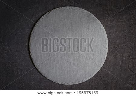 Empty round slate serving dish on a black stone background.