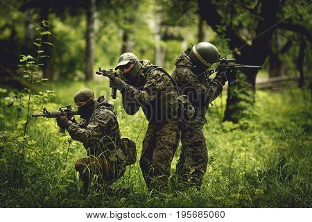 Strikeball players in camouflage with machine guns in woods among trees