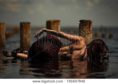 Young woman bathing in therapeutic water of mud estuary, next there are her reflection and wooden columns. Spa.