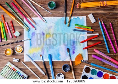 Painted paper, brushes, paints, colored pencils and prose stationery. Top view
