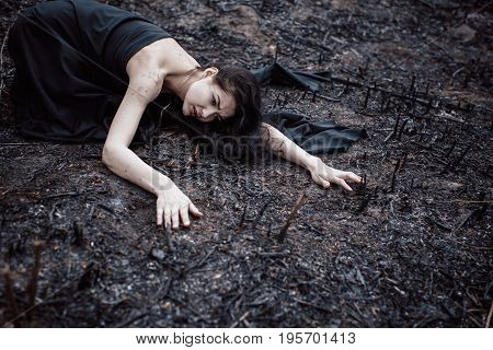 Sad girl sitting on the burned-out land. Concept of environmental disaster. Global problems with ecology. Young attractive multi-racial Asian Caucasian woman in black dress on nature