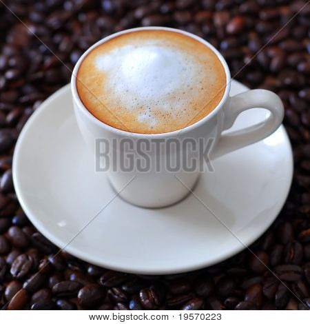 Una deliziosa tazza di caffè espresso/macciato con sfondo di chicchi di caffè
