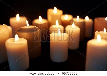 mourning and commemoration concept - candles burning in darkness over black background