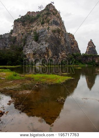 Wide angle view of the craggy mountains of Khao Ngu Stone Park and their reflections in the shallow lakes during a rainy day. Vertical orientation. Ratchaburi Thailand. Travel and nature concept.