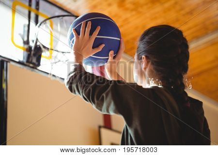 Side view of young woman practicing basketball while standing in court 