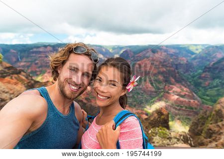 Selfie couple hikers in Waimea Canyon Hawaii hike taking self-portrait picture with camera phone having fun hiking in Kauai mountains, Hawaii. Woman and man in love taking photos on adventure travel.