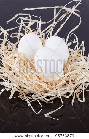 Three chicken eggs in the nest like On a black background