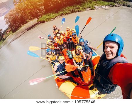 mountain Altai, RUSSIA - July 16, 2017: man in a helmet holds an action camera and makes selfie on the background of friends with oars, rafting