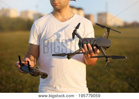Happy man shows You small compact drone and remote controller. Pilot holds quadcopter and RC in his hands on sunset