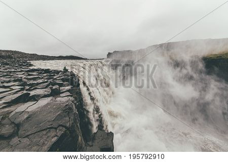 Tourist standing on extremely dangerous distance near Dettifoss waterfall in Vatnajökull National Park in Northeast Iceland.Extreme sports.Adrenalin.Possible accident.Hiking and climbing.
