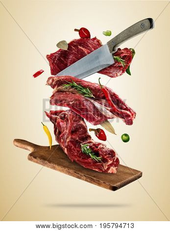 Flying pieces of raw steaks, with ingredients for cooking, served on woodenboard. Knife cutting the meat. Concept of food preparation in low gravity mode. High resolution image