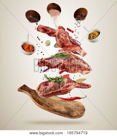 Flying pieces of raw pork steaks, with ingredients for cooking, served on woodenboard. Concept of food preparation in low gravity mode. Separated on soft background. High resolution image