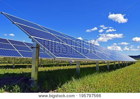 Solar panels on field. Clear sky with a few small clouds on background.