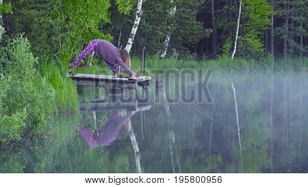 Young woman doing yoga exercises on the lake shore. Artha mukha svanasana