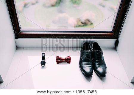 Groom's shoes, bow tie and watch on light window background. Preparation for wedding concept.