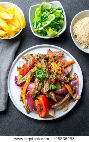 Peruvian dish Lomo saltado - beef tenderloin with purple onion, yellow chili, tomatoes served on white plate with french fries and rice. Top view