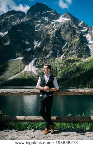 the groom stands on a background of mountains and lakes