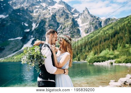 bride with the beautiful blue dress and groom hugging with views of the beautiful green mountains and lake with blue water