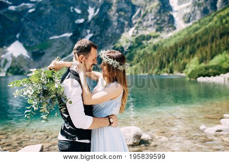 bride with the beautiful blue dress and groom hugging with views of the beautiful green mountains and lake with blue water
