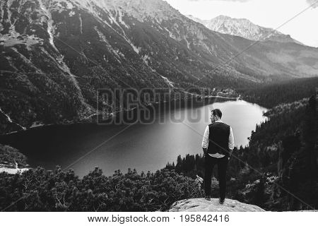 the groom stands on a background of mountains and lakes
