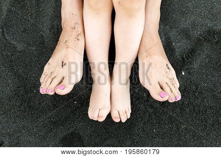Feet of mom and toddler in the black sand close-up. Summer, beach and family concept. Mom and child relaxing on the unique beach.