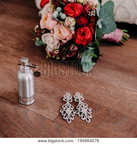 Beautiful bridal earrings and perfume on the wooden floor next to the wedding bouquet. Close-up