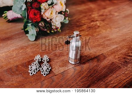 Bridal attributes such as elegant silver earrings with gem and perfume stand next to the bouquet. Preparation for wedding concept.