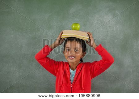 Portrait of young girl balancing books and apple on her head