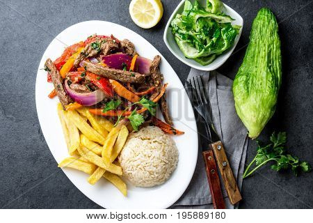 Peruvian dish Lomo saltado - beef tenderloin with purple onion, yellow chili, tomatoes served on white plate with french fries and rice. Top view