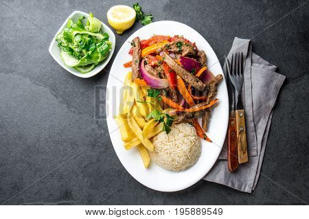 Peruvian dish Lomo saltado - beef tenderloin with purple onion, yellow chili, tomatoes served on white plate with french fries and rice. Top view