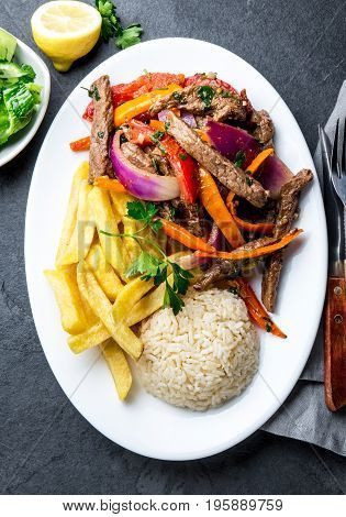 Peruvian dish Lomo saltado - beef tenderloin with purple onion, yellow chili, tomatoes served on white plate with french fries and rice. Top view